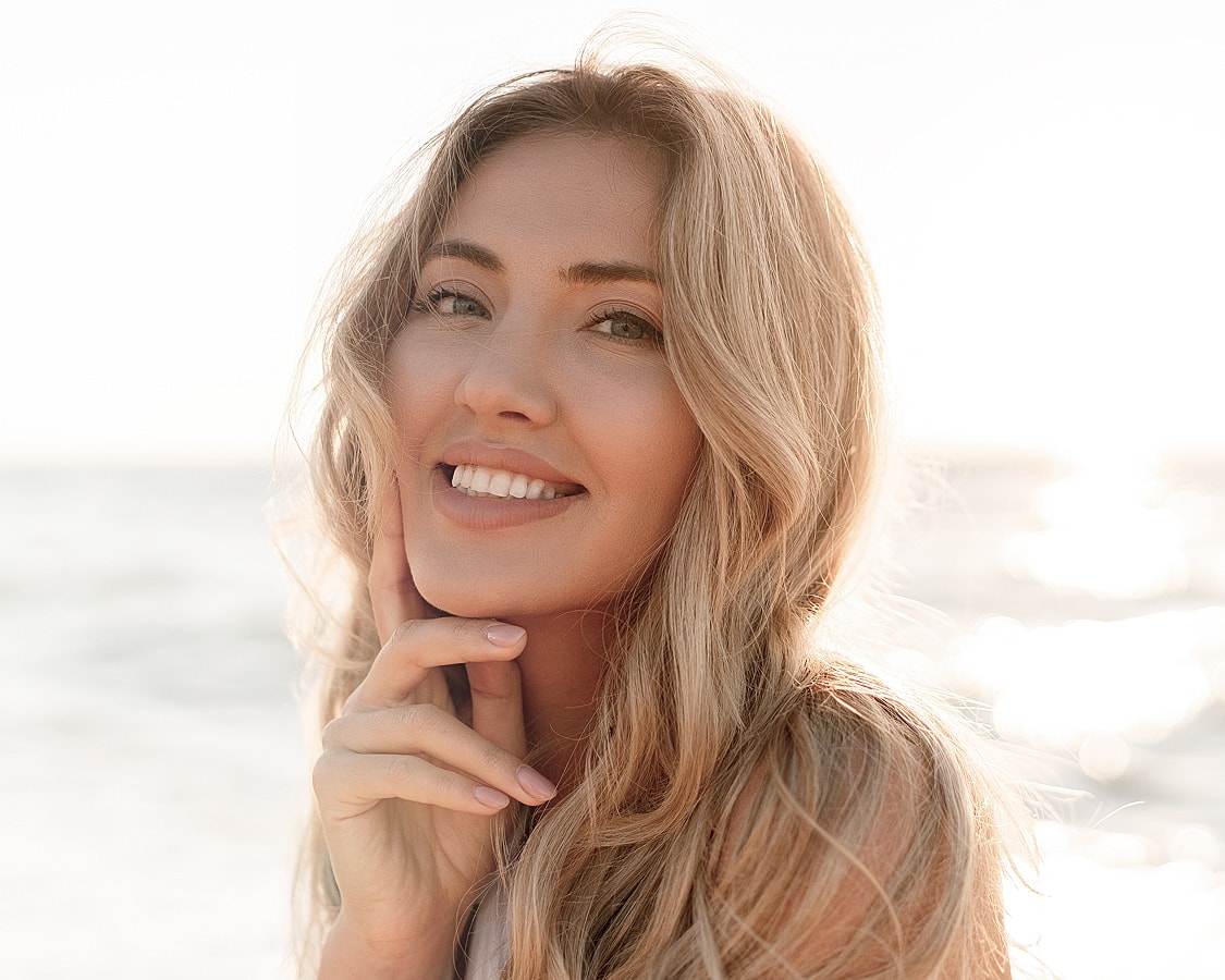 Smiling woman by the beach at sunset.
