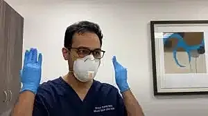 Healthcare worker adjusting mask and gloves.