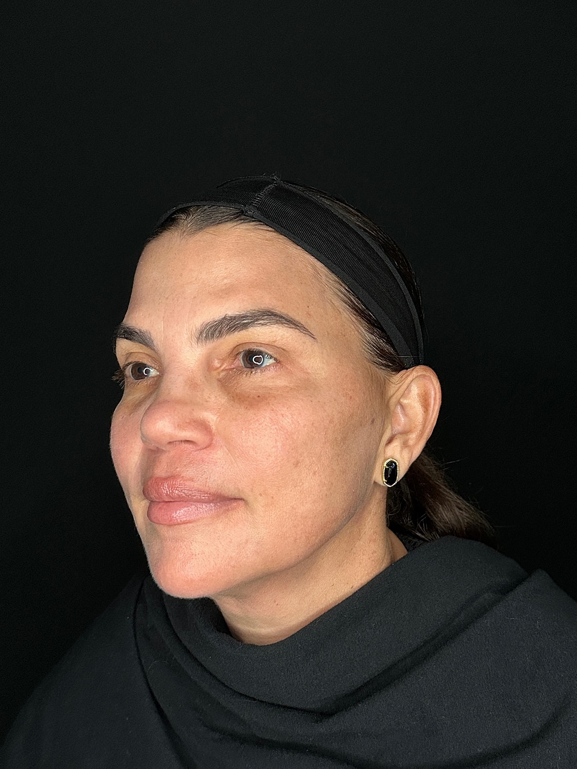 Woman with headband and earrings against black background.