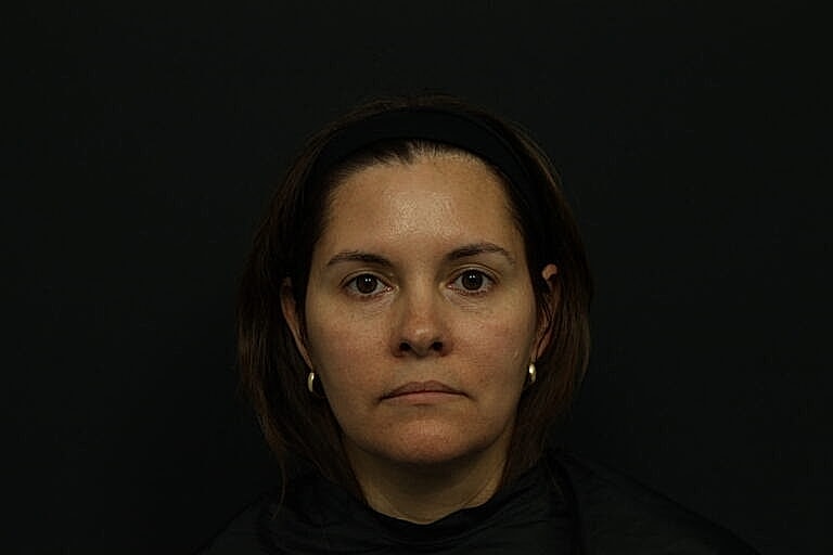 Woman with a neutral expression against a dark background.
