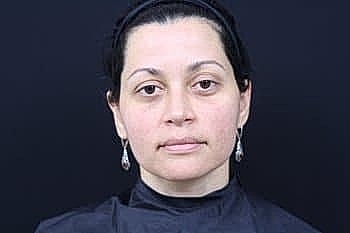 Woman with earrings and neutral expression, black background.