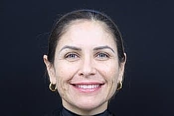 Smiling woman with dark hair against black background.