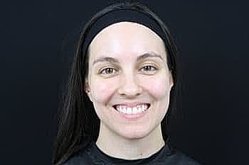 Smiling woman with long hair against black background.