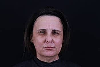 Serious woman with neutral expression against dark background.