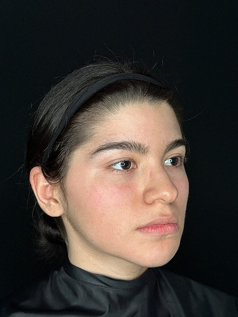 Young woman with a neutral expression, dark background.