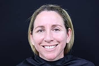 Smiling woman with short hair, black background.