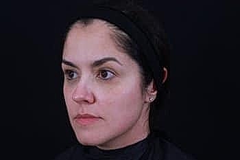 Woman with a neutral expression against a dark background.
