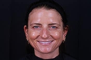 Smiling woman with dark hair against black background.