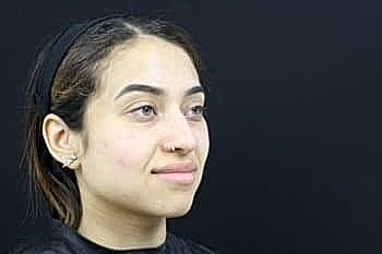 Young woman with a neutral expression on black background.