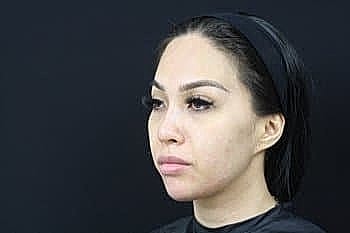 Woman with makeup, facing left against black background.