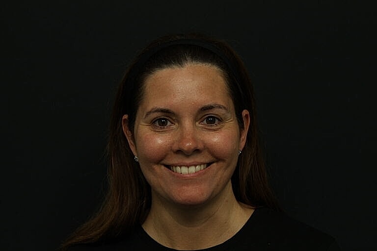 Smiling woman with long brown hair, dark background.