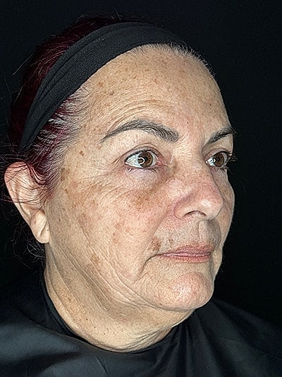 Middle-aged woman with facial expression against dark background.
