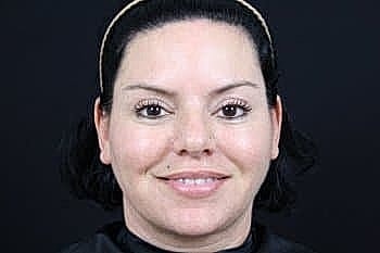 Woman with short hair smiling against black background.