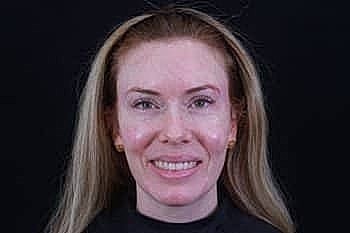 Smiling woman with long hair, black background.