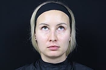 Woman with short hair looking upward against black background.