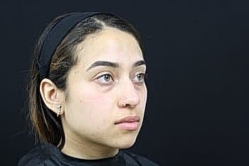 Young woman with headband against black background.