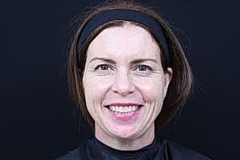 Smiling woman with brown hair against black background.