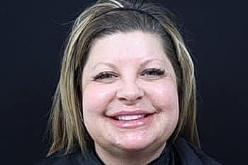 Smiling woman with long hair against black background.