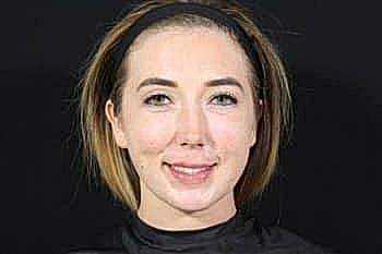 Smiling person with short hair against black background.