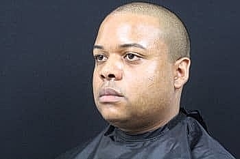 Man with a close-cropped hairstyle in barber's cape.