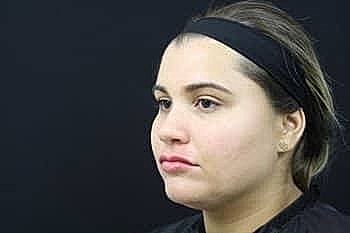 Woman with neutral expression against black background.