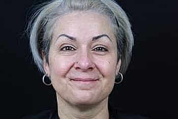 Smiling woman with light gray hair and earrings.