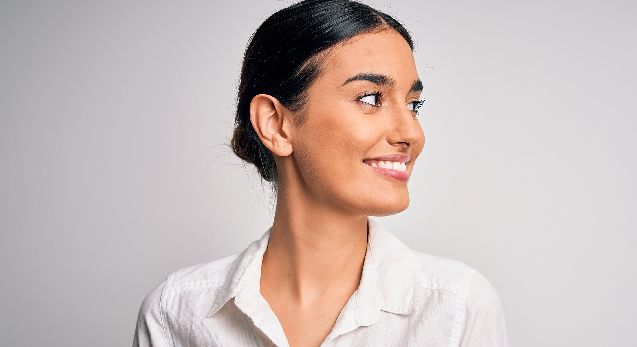 Smiling woman looking to the side, neutral background.
