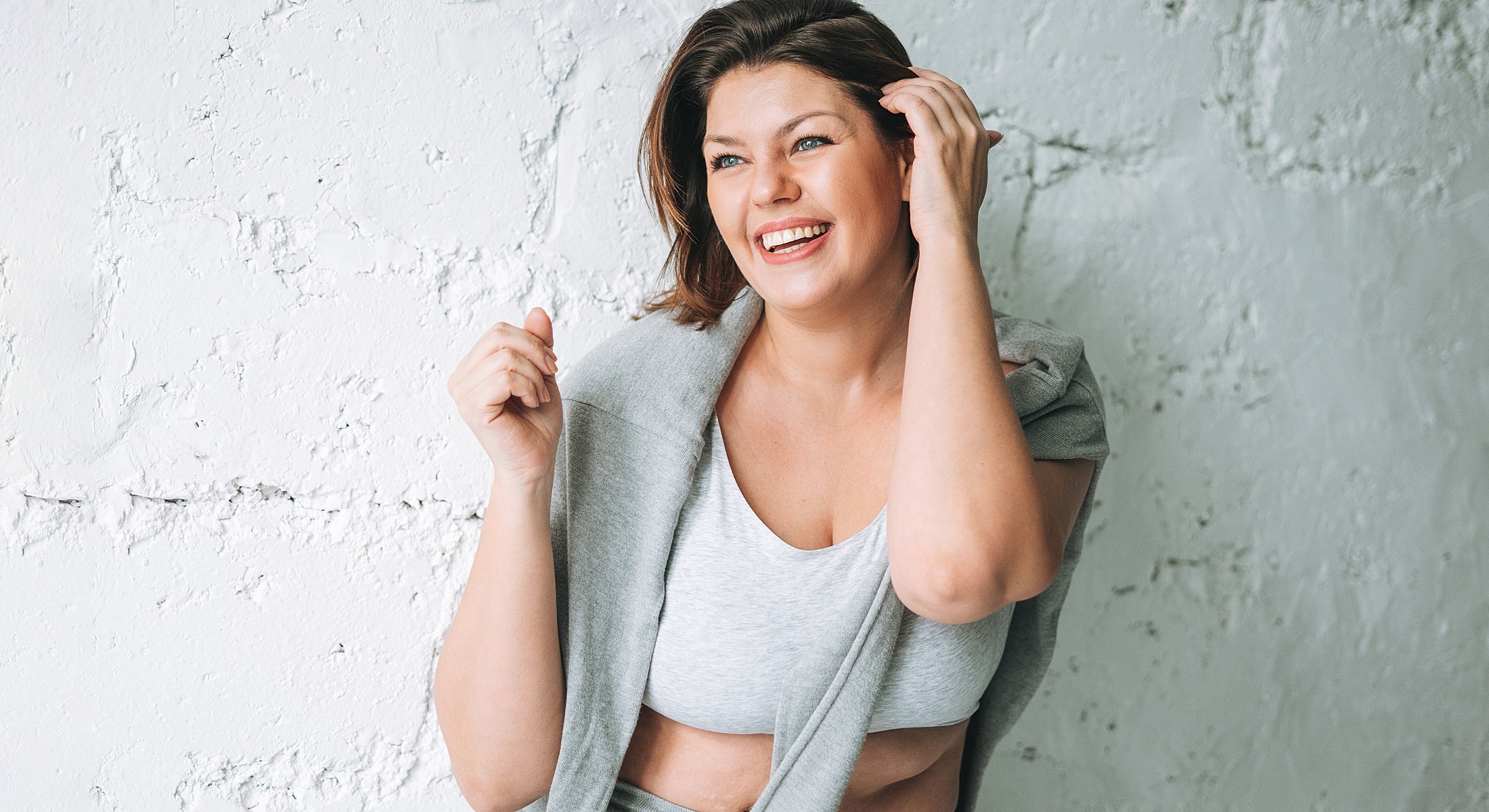 Smiling woman in casual outfit against textured wall.